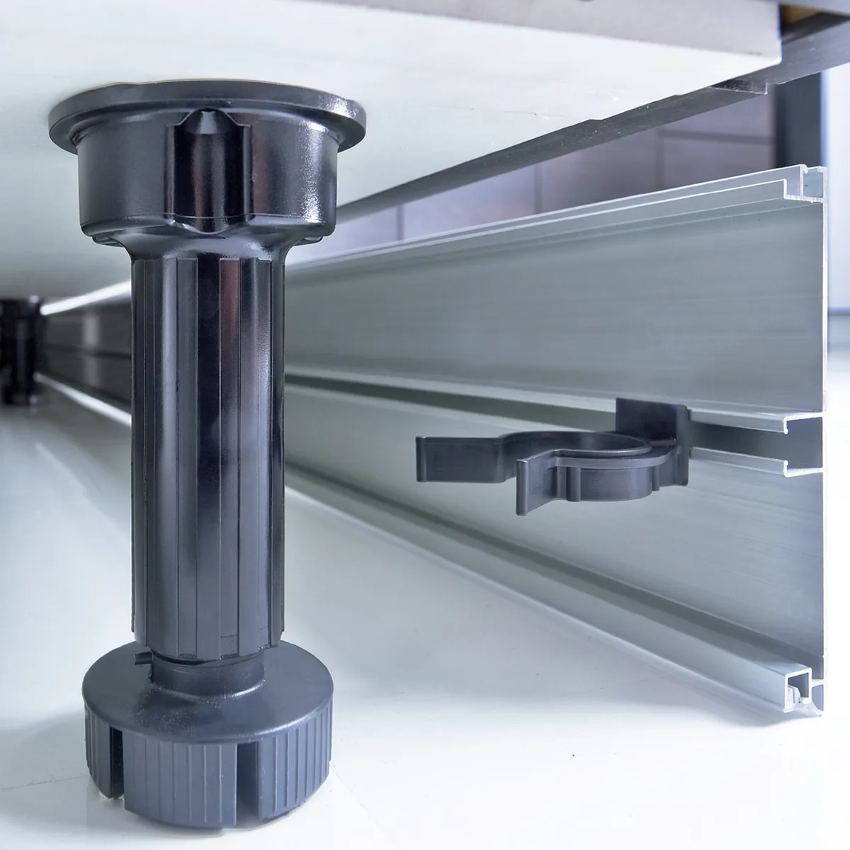 Clap N Fit clip-on plinth fixing Black adjustable cabinet leg with a plinth clip holding a grooved aluminium plinth profile under a white cabinet