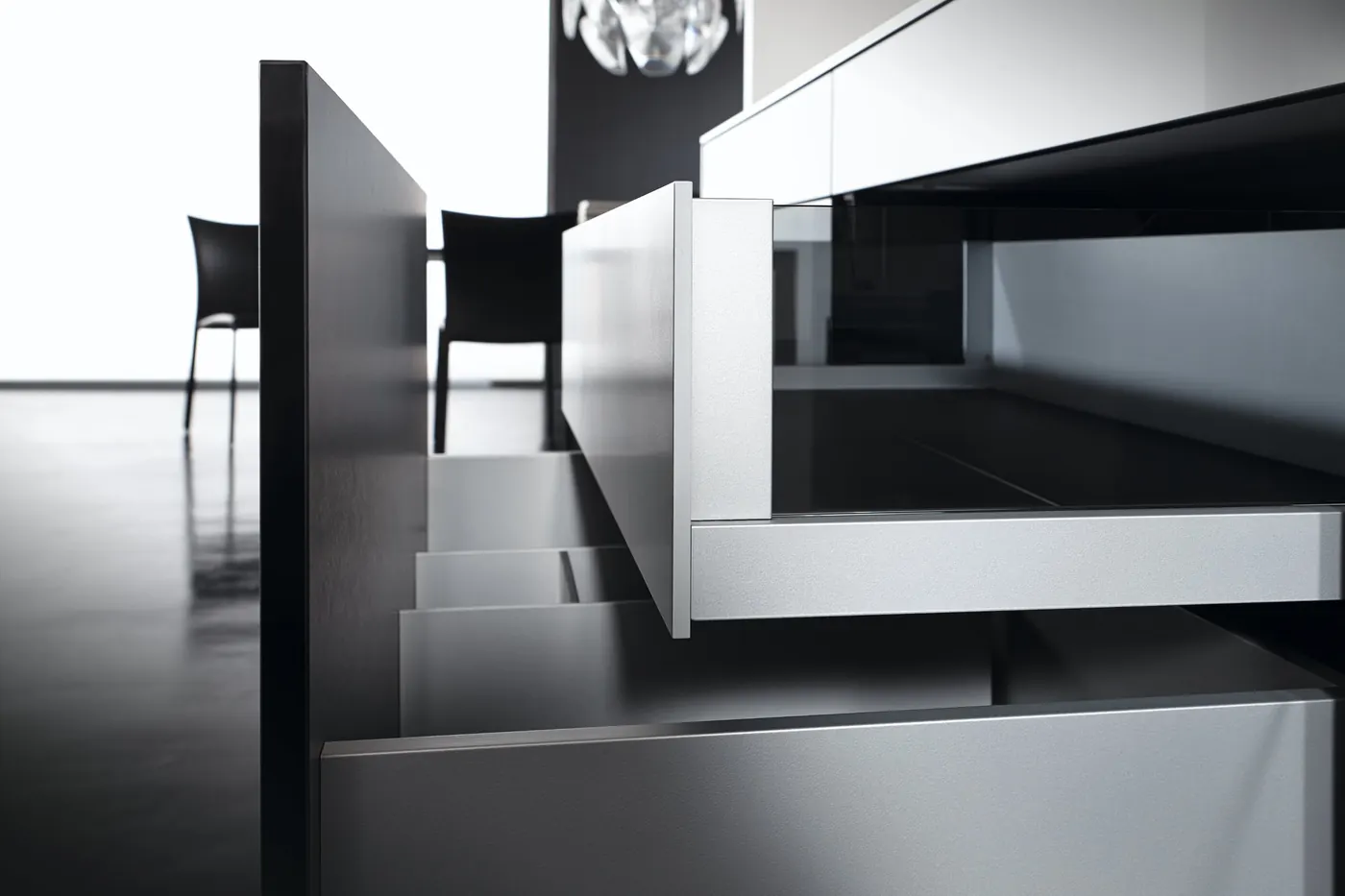 Low-angle view of a slim metal drawer side and front with several drawers open in a black and white kitchen