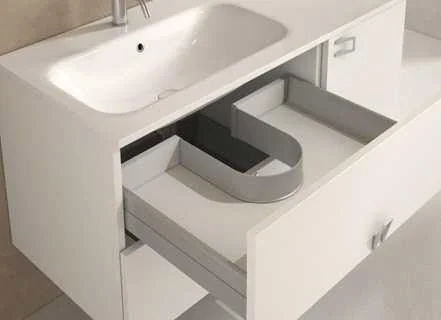 Open drawer under a white basin with a grey U-shaped surround built around the plumbing space