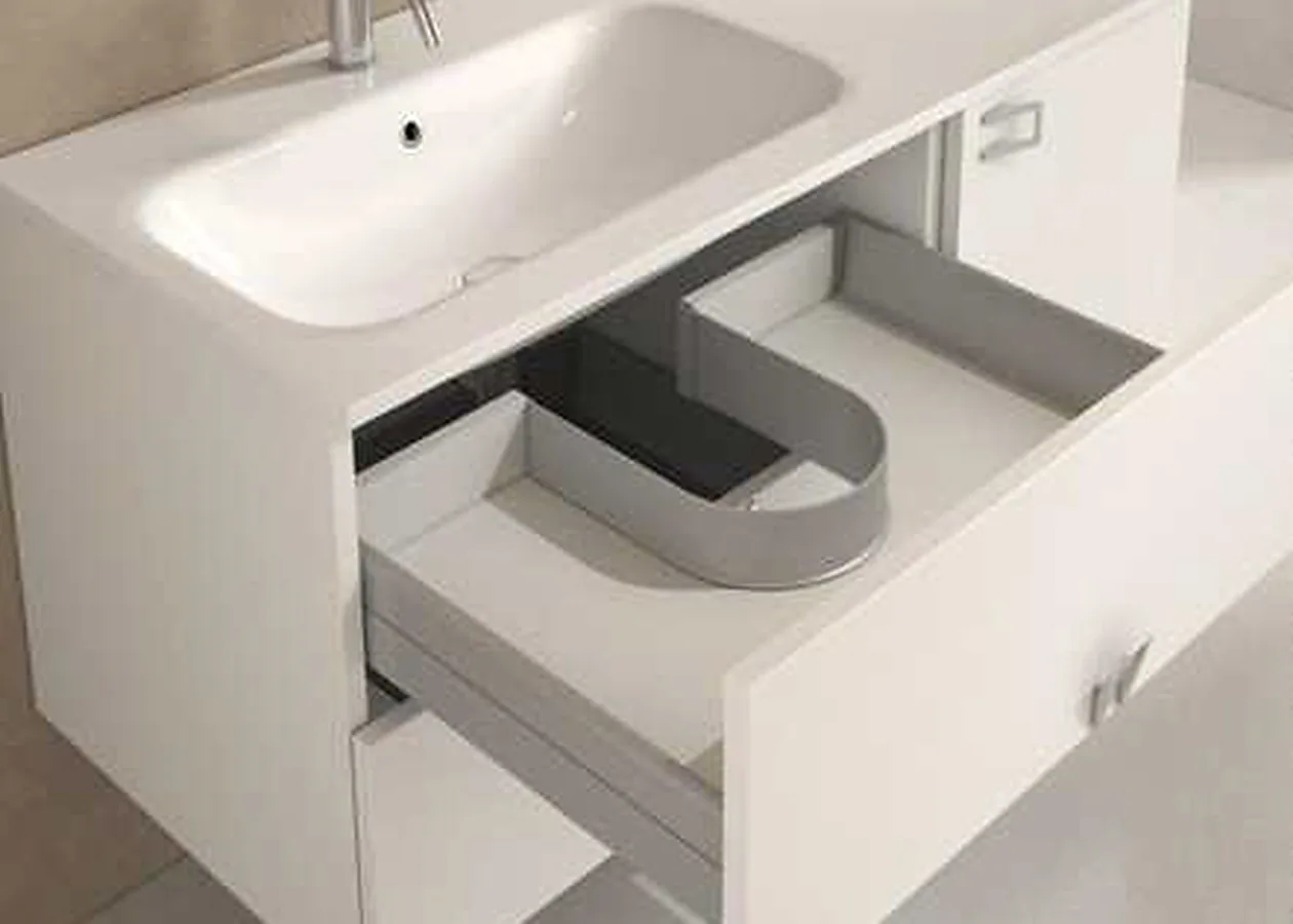 Under-sink drawer with a U-shape guard fitted around the waste pipe cut-out in a white vanity unit Under-sink drawer with a U-shape guard fitted around the waste pipe cut-out in a white vanity unit